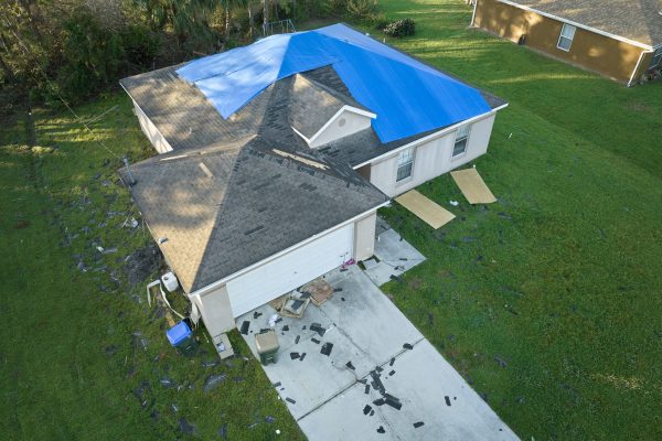 Top view of leaking house roof covered with protective tarp sheets against rain water leaks until replacement of asphalt shingles. Damage of building rooftop as aftermath of hurricane Ian in Florida.